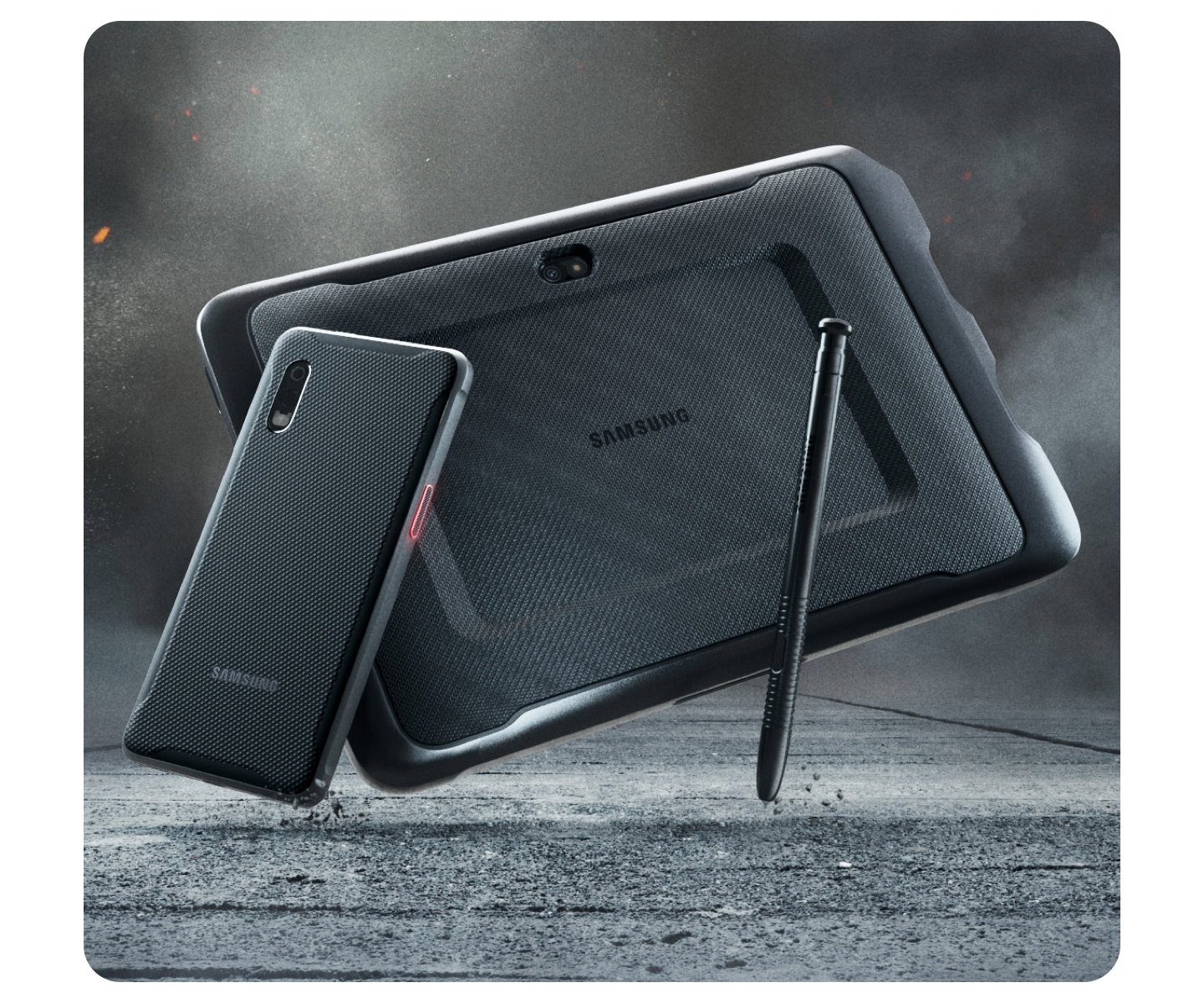 Rugged Samsung tablet, rugged Samsung smartphone & black S Pen falling on a grey concrete floor with grey dust clouds behind