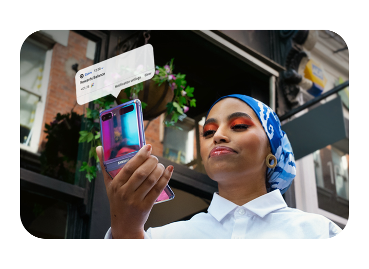 A woman looks down at her Galaxy Z Fold2 smartphone which she is holding at arm's length while walking down a street A woman looks down at her Galaxy Z Fold2 smartphone which she is holding at arm's length while walking down a street
