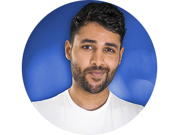 Headshot of Arun Maini against a blue background. He's wearing a T-shirt and smirking at the camera