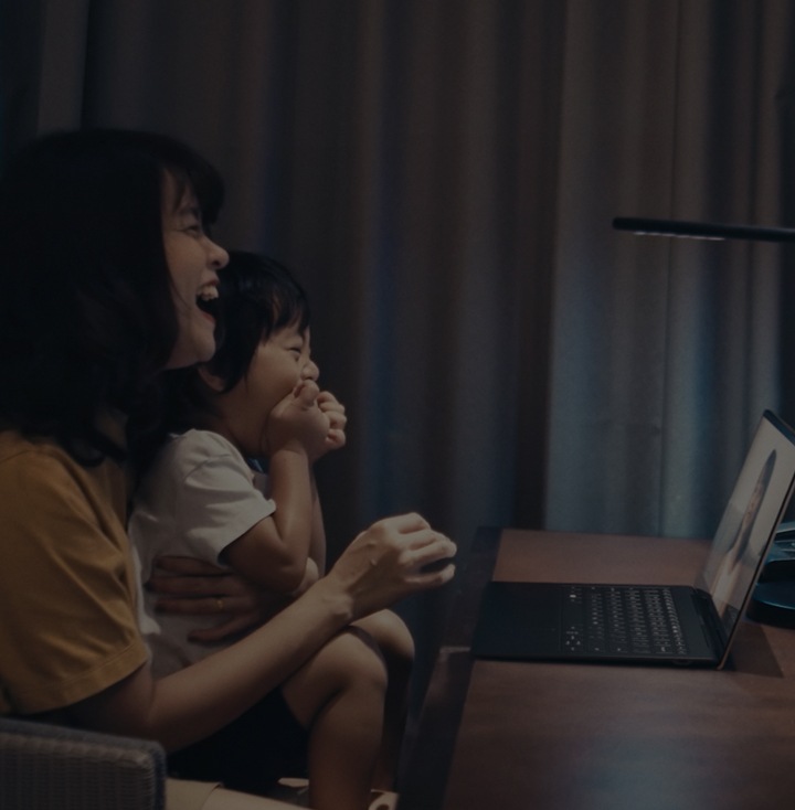 A girl and her mom looking at the laptop screen for video call and laughing together.