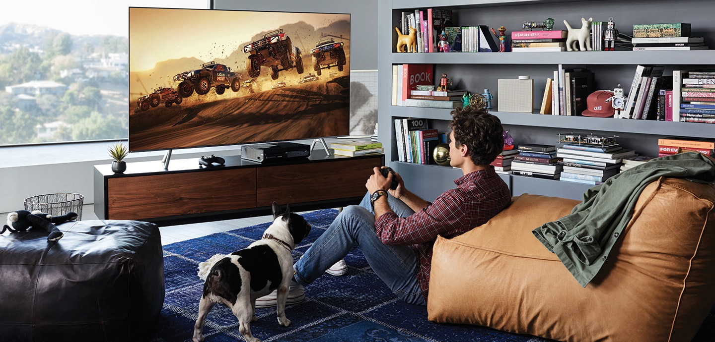A young man is playing game with QLED TV. Players can complete their gaming experience with its big screen and 4K picture quality with HDR.