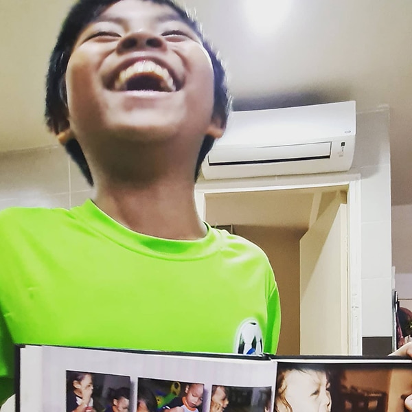 A boy in green shrit holding a photo album and smiling