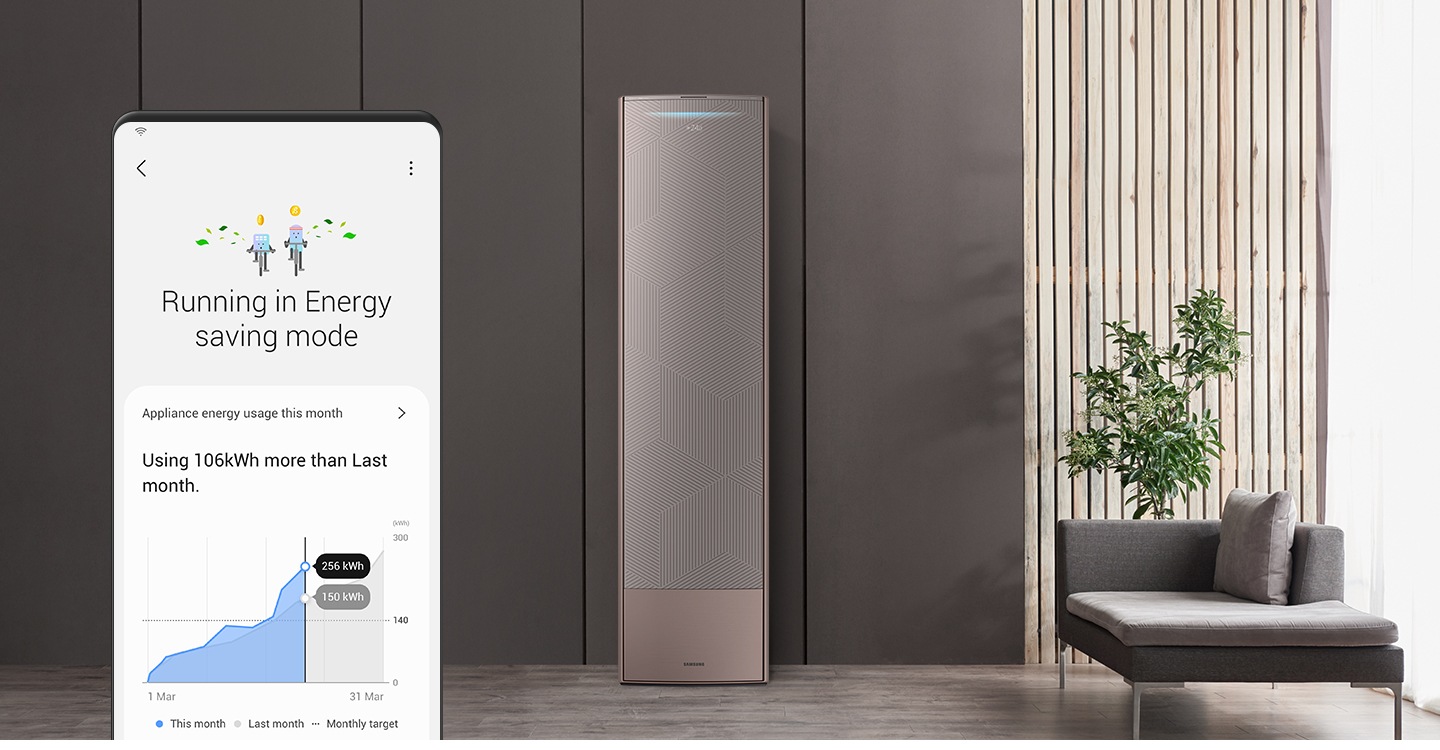 Máy điều hòa không khí thông minh ở nền trung tâm và màn hình Galaxy ở tiền cảnh bên trái. Màn hình hiển thị tính năng SmartThings Energy ở chế độ tiết kiệm năng lượng và biểu đồ so sánh mức sử dụng năng lượng của tháng hiện tại và tháng trước.