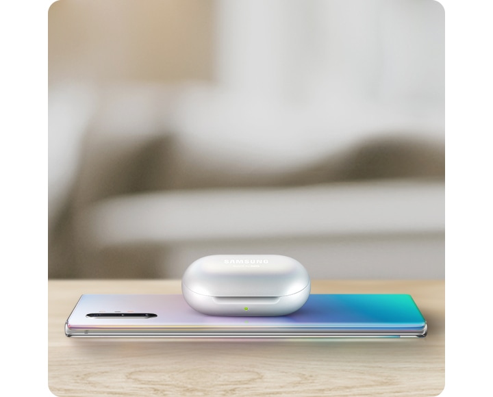 Galaxy Note10+ laying facedown on a table with Galaxy Buds charging on top via Wireless PowerShare.