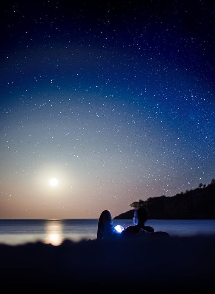 Background image of a person sitting outside in the dark, looking at a glowing Galaxy Note9.