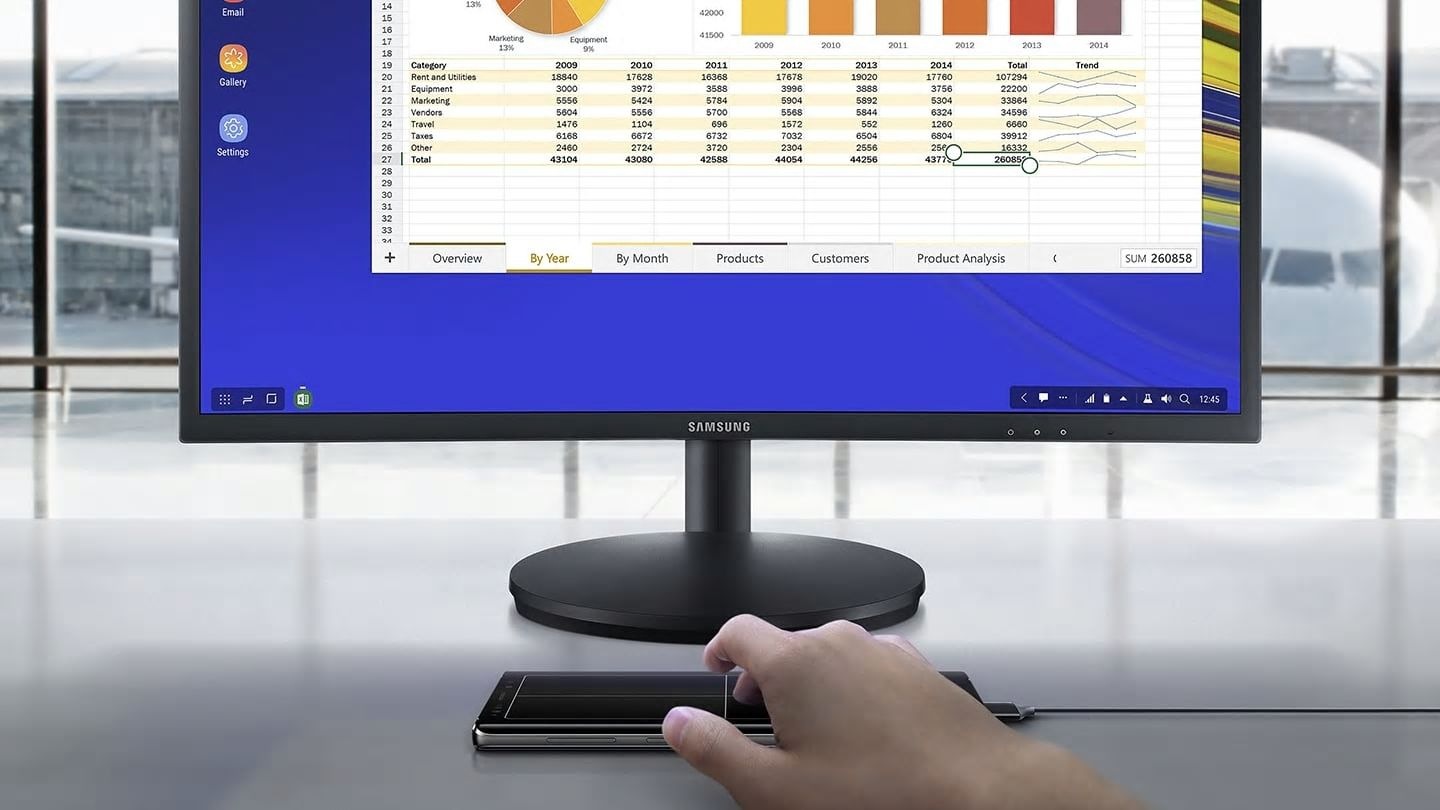 "Simulated image of a person using Galaxy Note9 connected to Samsung DeX via a single cable, looking at a spreadsheet on the connected monitor and using Galaxy Note9 as a touchpad