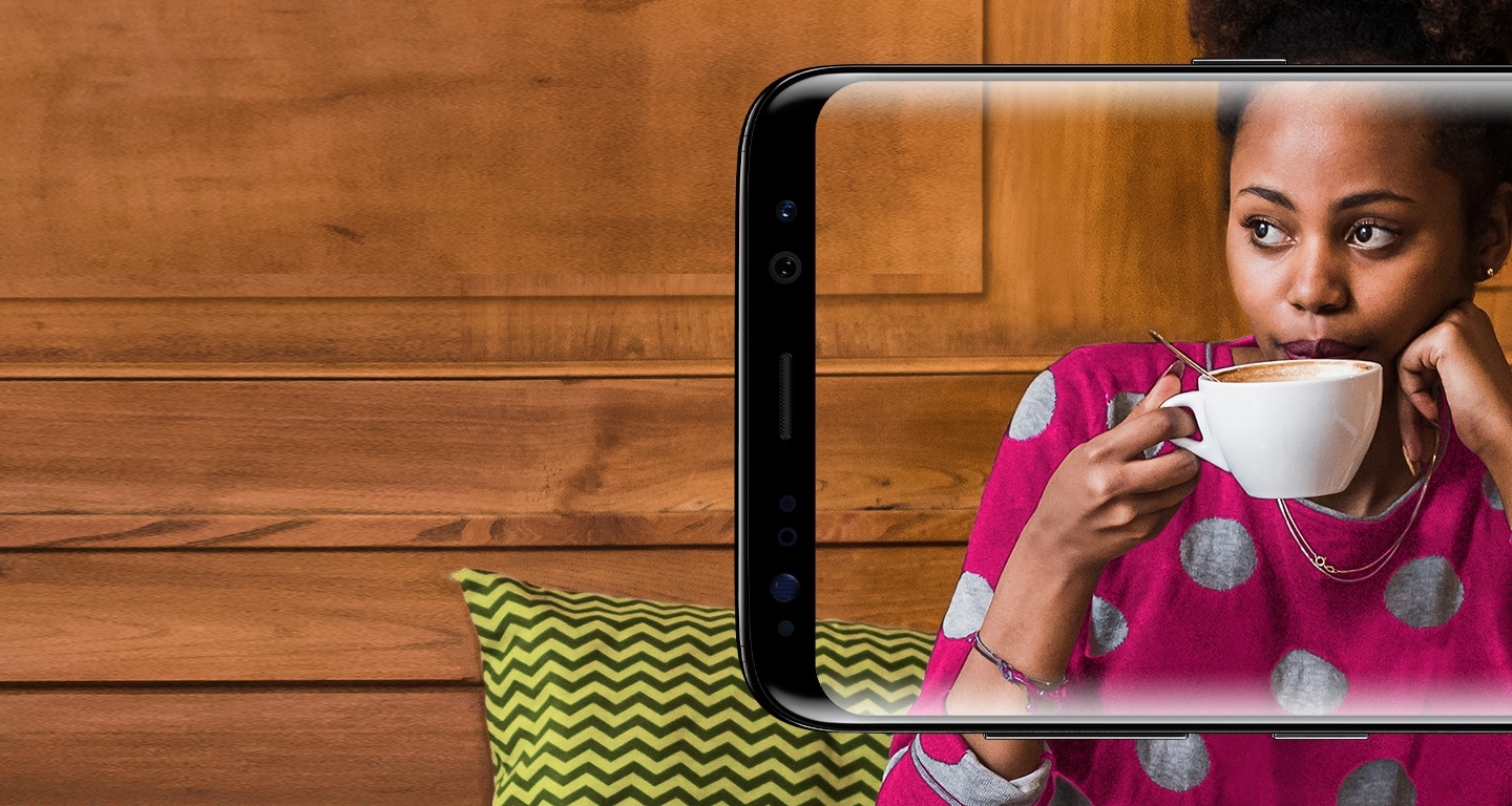 A woman taking a sip of her coffee in a café seen through a Samsung Galaxy S8 screen