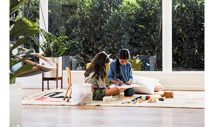 Two young girls in the living room sit drawing and playing with colors and blocks as a coloring activity.