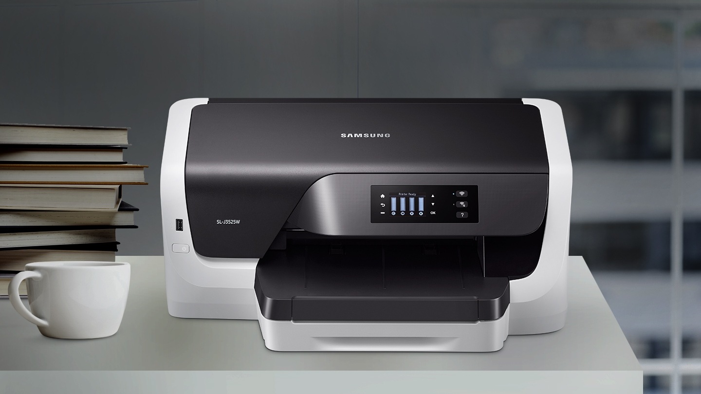 어두운 책상에 프린터 제품이 올려져있고 왼쪽에는 커피잔과 책이 놓여져있다.