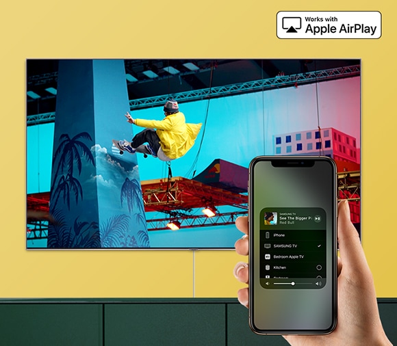 노란색 벽면을 배경으로 이미지 상단에 애플 에어플레이 로고가 보이고, 중앙에는 TV가 보입니다.  스마트폰에서 재생한 콘텐츠가 TV에서도 동일하게 재생되는 모습을 보여주고 있습니다.