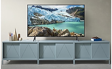 회색 벽을 배경으로 민트색 TV 수납장 위에 빙하와 바다 영상이 보이는 TV 제품이 놓여져 있습니다.