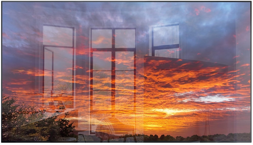제품의 베젤과 화면만 보여지고 있으며, 화면 안에는 노을진 하늘에 붉은 구름과 파란색 구름이 보여지고 중앙에 가로 선이 있으며 좌측에는 빛이 반사되어 창문이 비추고 있습니다.