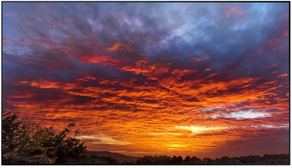 제품의 베젤과 화면만 보여지고 있으며, 화면 안에는 노을진 하늘에 붉은 구름과 파란색 구름이 보여지고 있습니다.