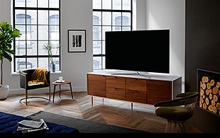 창밖이 훤희 보이는 거실에 쇼파와 검정색 강아지가 있습니다. 쇼파 앞에는 벽에 제품이 걸려있으며 제품하단에는 작은 선반이 있습니다.