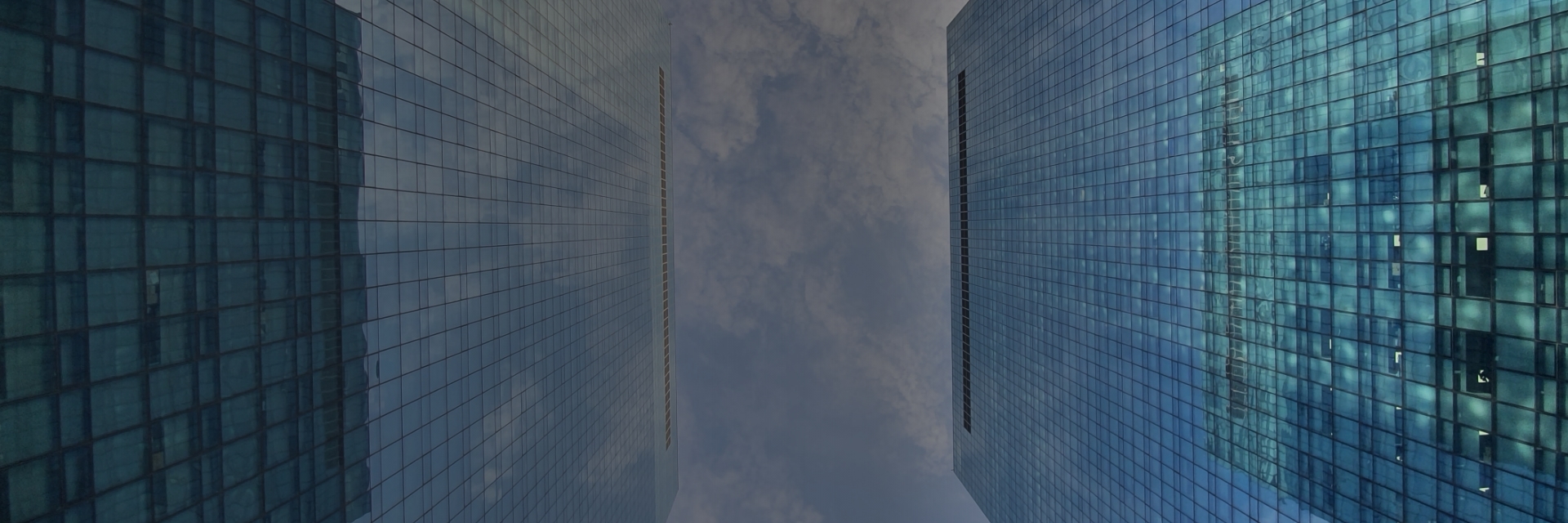 반사되는 유리 외벽이 있는 높은 사무실 빌딩 사이로 아래에서 하늘을 올려다보는 사진.