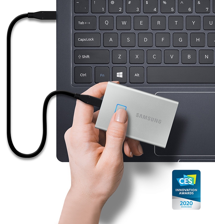 노트북 포트와 연결된 실버 색상의 포터블 SSD T7 Touch 제품을 쥔 손이 있고 제품 우측 하단에 CES 수상 로고가 보입니다.