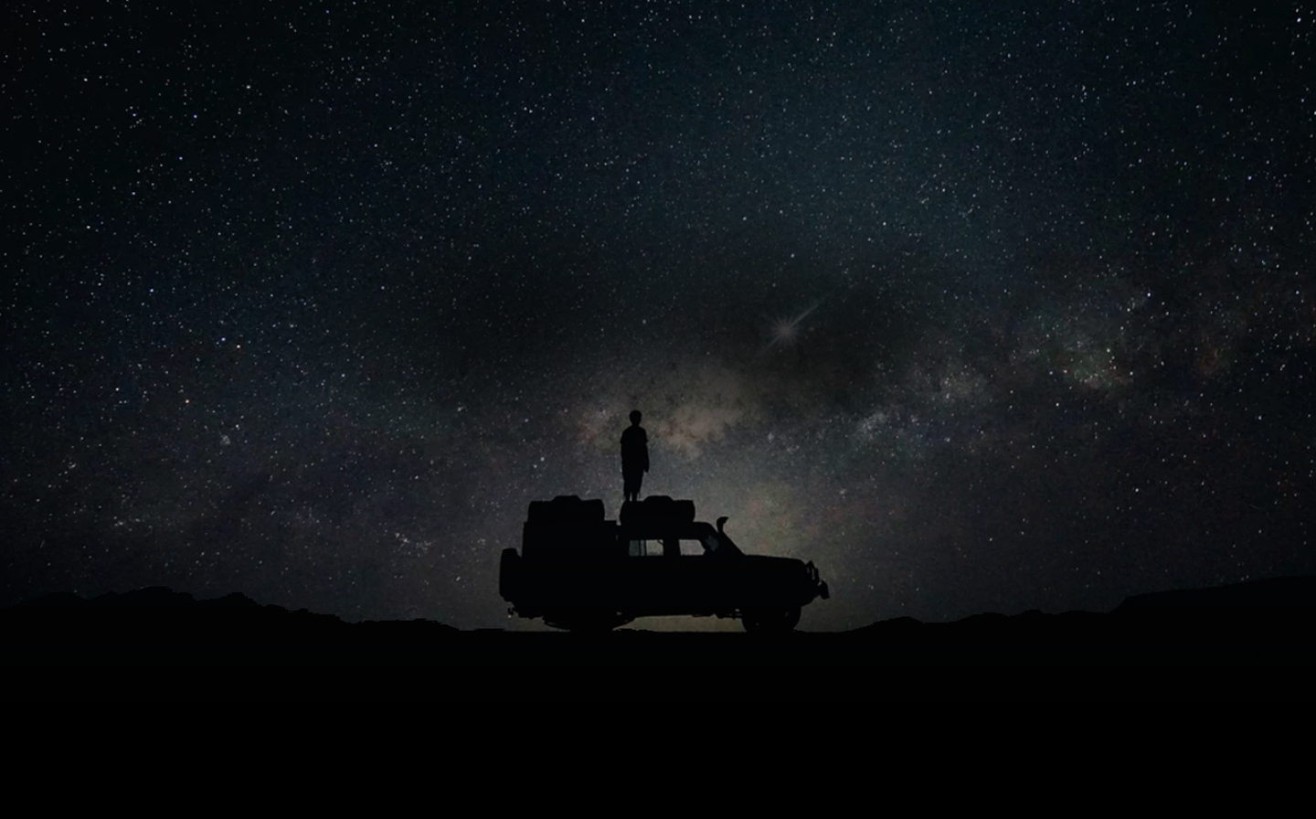 별빛이 장관을 이루는 밤 하늘을 배경으로 한 사람이 차 위에 서서 하늘을 바라보고 있습니다. 배경에는  '5G 히스토리'라는 텍스트와 '3G 기술부터 초고속 5G 시대까지'라는 텍스트가 위아래로 나란히 적혀 있습니다.