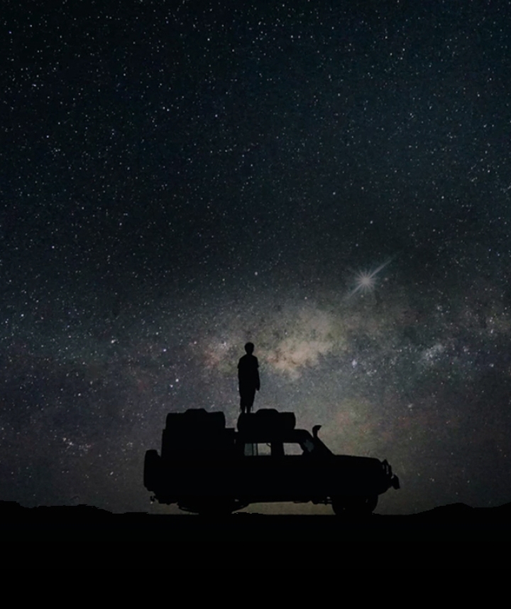 별빛이 장관을 이루는 밤 하늘을 배경으로 한 사람이 차 위에 서서 하늘을 바라보고 있습니다. 배경에는  '5G 히스토리'라는 텍스트와 '3G 기술부터 초고속 5G 시대까지'라는 텍스트가 위아래로 나란히 적혀 있습니다.