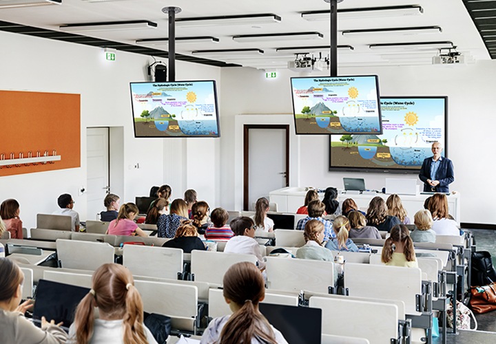 대형 강의실의 모습입니다. 제일 앞에는 WAF 전자칠판이 설치되어 있으며, 선생님이 수업을 진행중인 모습입니다. 강의실의 천장에는 다른 TV 화면을 통해 벽면의 WAF 전자칠판과 동일한 화면을 출력하여 보여주고 있는 모습입니다.