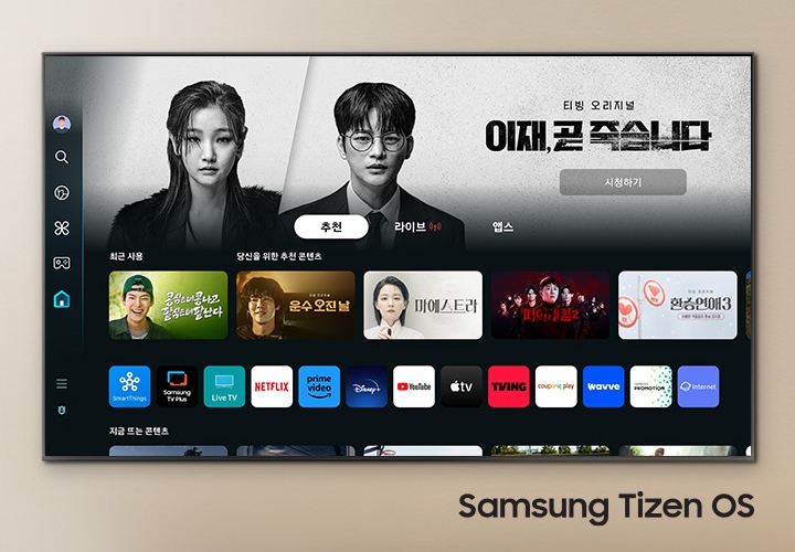 벽에 TV가 설치되어 있으며, 화면 속에는 이재 곧 죽습니다 드라마 메인 화면이 보이고 있으며, 그 하단에는 여러 예능과 드라만 메인 화면이 보입니다. TV 오른쪽 하단에는 Samsung Tizen OS 문구가 기재되어 있습니다.