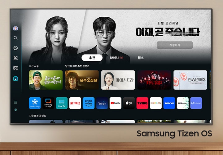벽에 TV가 설치되어 있으며, 화면 속에는 이재 곧 죽습니다 드라마 메인 화면이 보이고 있으며, 그 하단에는 여러 예능과 드라만 메인 화면이 보입니다. TV 오른쪽 하단에는 Samsung Tizen OS 문구가 기재되어 있습니다.