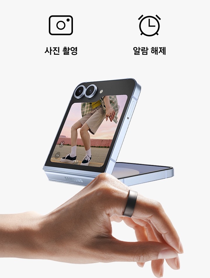 갤럭시 링을 착용한 손이 있고 손가락으로 꼬집는 듯한 동작을 하고 있습니다. 카메라가 열린 갤럭시 Z 폴드6가 접혀져 있습니다. 스마트폰 위에 2개의 아이콘이 있고 각각 카메라 앱과 알람 끄기입니다.