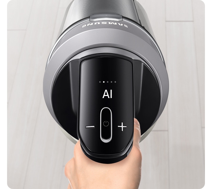 밝은 베이지 톤의 원목 마루가 깔린 바닥이 보입니다. 가운데는 BESPOKE AI 제트 Lite 280W 를 잡고 있는 손과 청소기 헤드가 확대되어 보입니다. 청소 중인 제트의 알림 창에는 AI 문구가 보입니다.