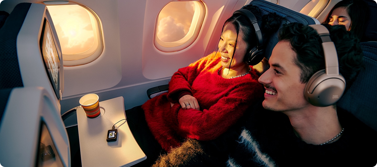 헤드폰을 착용한 남녀가 비행기 기내 엔터테인먼트 시스템에 트랜스미터를 연결하여 영상을 보고 있습니다.