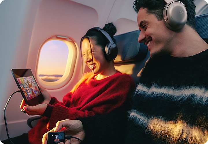 비행기 내에서 헤드폰을 착용한 남녀가 트랜스미터와 태블릿을 연결하여 영상을 보고 있습니다.