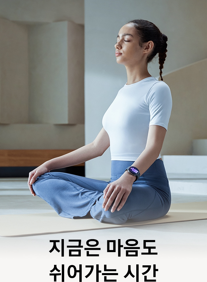 한 여성이 실내에 가부좌 자세로 앉아 눈을 감고 있습니다. 손목에는 갤럭시 워치8을 착용하고 있습니다.
