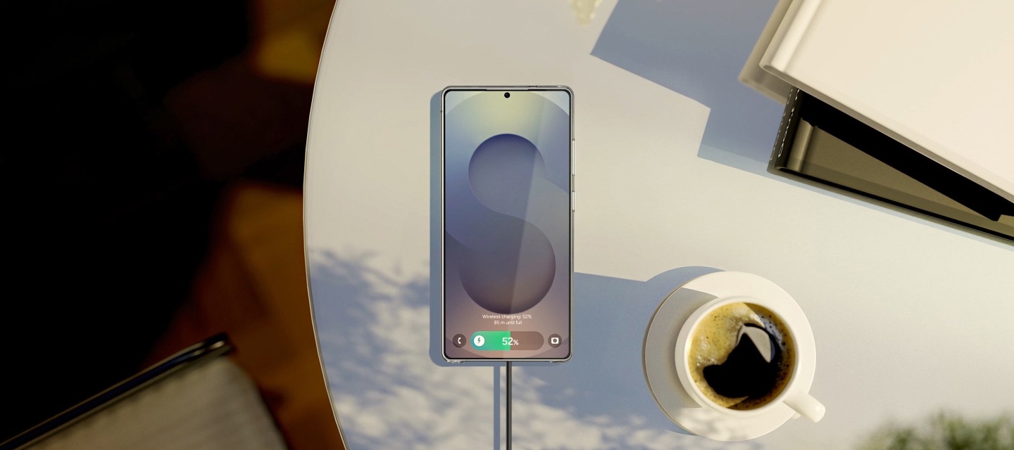 원형 탁자에 놓인 마그넷 무선 충전기가 부착된 스마트폰과 커피잔, 책들이 탑뷰로 보이고 있습니다.