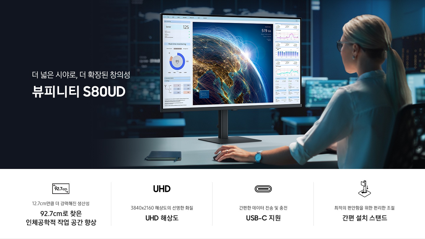 여성이 모니터를 응시하며 작업을 하고 있는 모습입니다. 모니터에는 지구모양과 다양한 그래프가 있습니다.