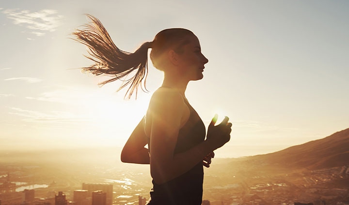 떠오르는 태양을 배경으로 한 여성이 달리고 있습니다. 여성의 머리카락이 바람에 흩날리며 역동적으로 움직입니다.