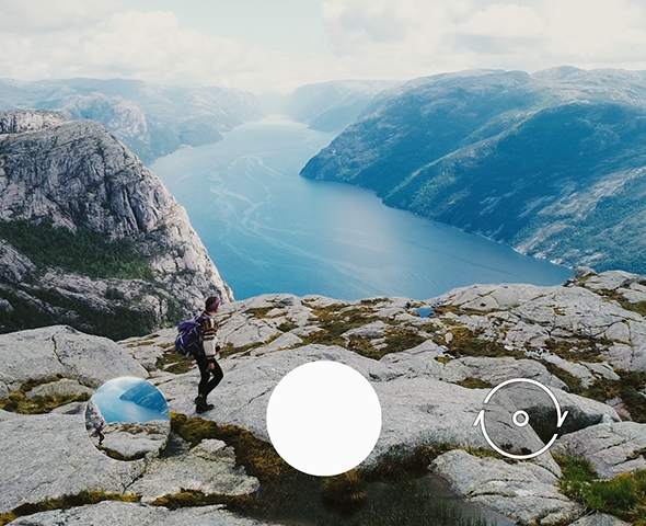 Person with backpack walking on a rock-lined path above a beautiful fjord.