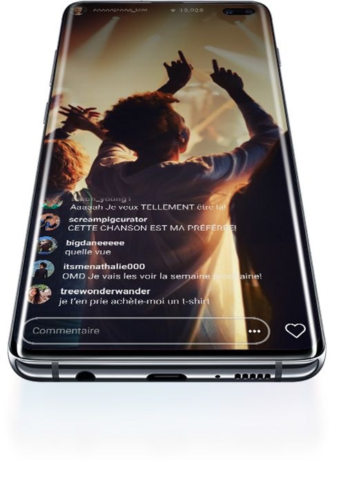 Galaxy S10+ posé sur le dos, vu dans un angle fermé du dessous. Au départ, un logo S10 prismatique apparaît à l’écran, puis se change en icône Wi-Fi prismatique, puis présente finalement un concert diffusé en direct avec les commentaires sur l’écran.