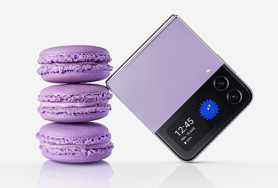 Un Galaxy Z Flip4 Violet Bora plié vu de l’écran extérieur. Il repose sur une pile de trois macarons de la même couleur. La taille de l’appareil plié est similaire à celle des trois macarons empilés.