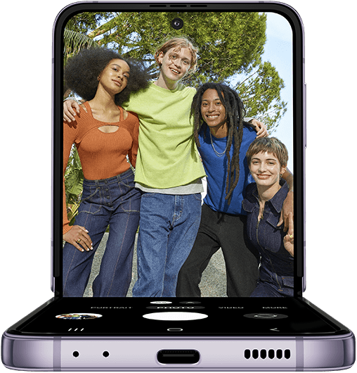 Galaxy Z Flip4 en mode FlexCam. L’application de l’appareil photo est affichée sur l’écran principal et montre une photo de groupe prise à un angle bas. Un groupe d’amis pose pour une photo. Situé sur le sol devant eux, un Galaxy Z Flip4 en mode FlexCam prend leur photo. Les amis peuvent voir l’aperçu de la photo sur l’écran principal en mode Flex.