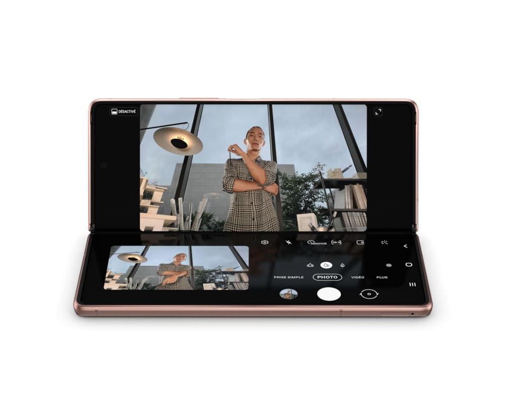 Galaxy Z Fold2 Bronze Mystique en mode Flex. L’écran passe à l’application Appareil photo et montre un homme prenant un selfie en mains-libres avec le mode Capture View. Il obtient une prévisualisation élargie de la photo qu’il vient de prendre.