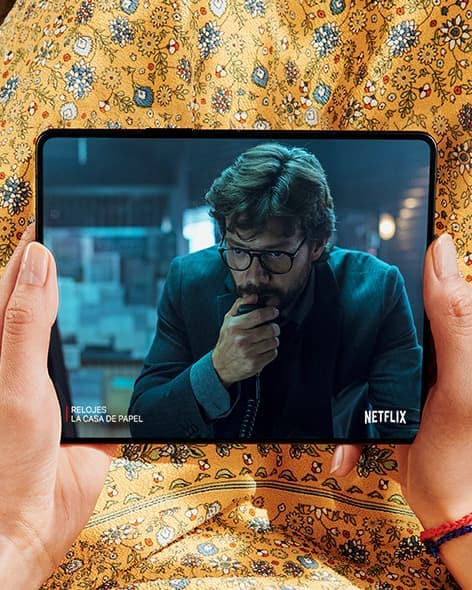 Des mains tenant le Galaxy Z Fold3 5G, déplié. L’écran principal affiche une scène d’une vidéo Netflix d’un homme appuyant sa main sur son visage.