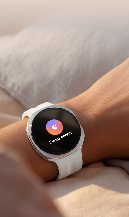 Uma pessoa está a dormir na cama com o Galaxy Watch9 no pulso. A funcionalidade de rastreio do sono é exibida no ecrã, e a pessoa tem um sorriso subtil no rosto, indicando que o programa de Coaching do Sono ajudou a melhorar os seus padrões e hábitos de sono, levando a um sono mais reparador.