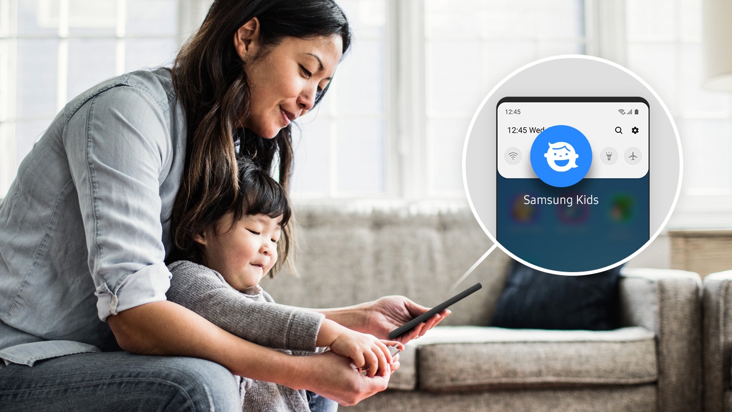Imagen simulada de una mujer con su hijo en su sala de estar. La mujer sostiene un teléfono inteligente, y hay una superposición simulada de su pantalla con el icono de Samsung Kids agrandado, mostrando cómo puedes acceder fácilmente a Samsung Kids en el panel Quick.