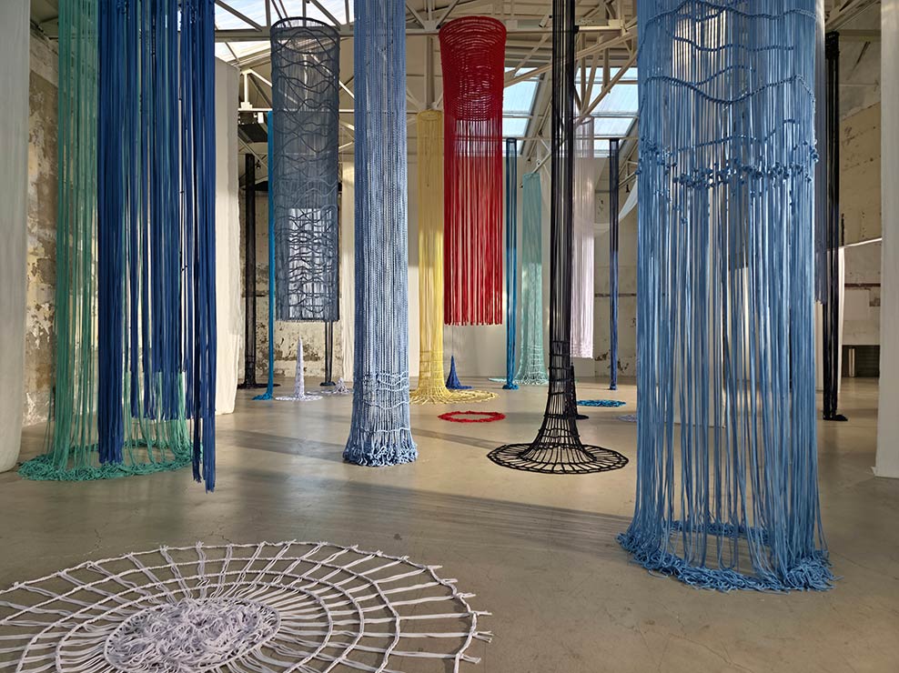 Fotografía amplia dentro de un museo con coloridas instalaciones de cuerdas. Los colores son brillantes y los detalles son claros.