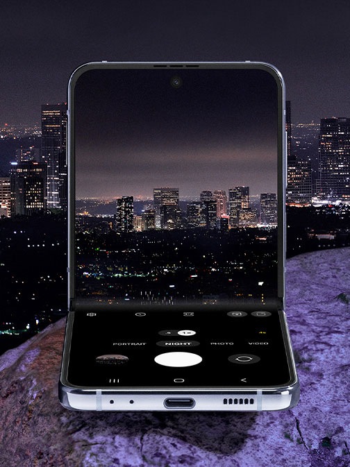 Galaxy Z Flip4 in Flex mode. The camera is seen on the Main Screen in Night mode. It is showing a preview of a city skyline at night. Night mode makes the color and details of the city lights vivid and clear.