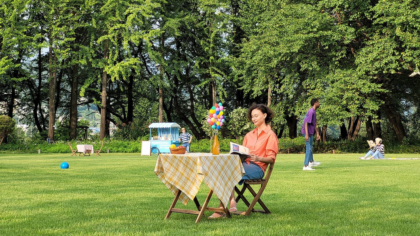Tri puta uvećana fotografija koja približava ženu koja sjedi sama za stolom u pozadini fotografije koja je uvećana jednom.