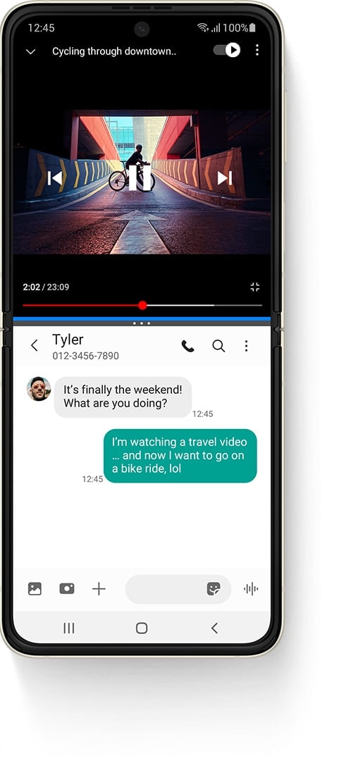 Galaxy Z Flip3 5G rasklopljen u multiaktivnog prozoru, sa YouTube videom na vrhu, čiji je naziv 'Biciklom kroz centar grada' i osobom koja stoji na biciklu na rampi. Aplikacija Poruke na dnu i primljena SMS poruka od Tyler kaže" Napokon je vikend! Šta radiš?" Poslana tekstualna poruka glasi: Gledam video sa putovanja... i sada želim ići na vožnju biciklom, lol"