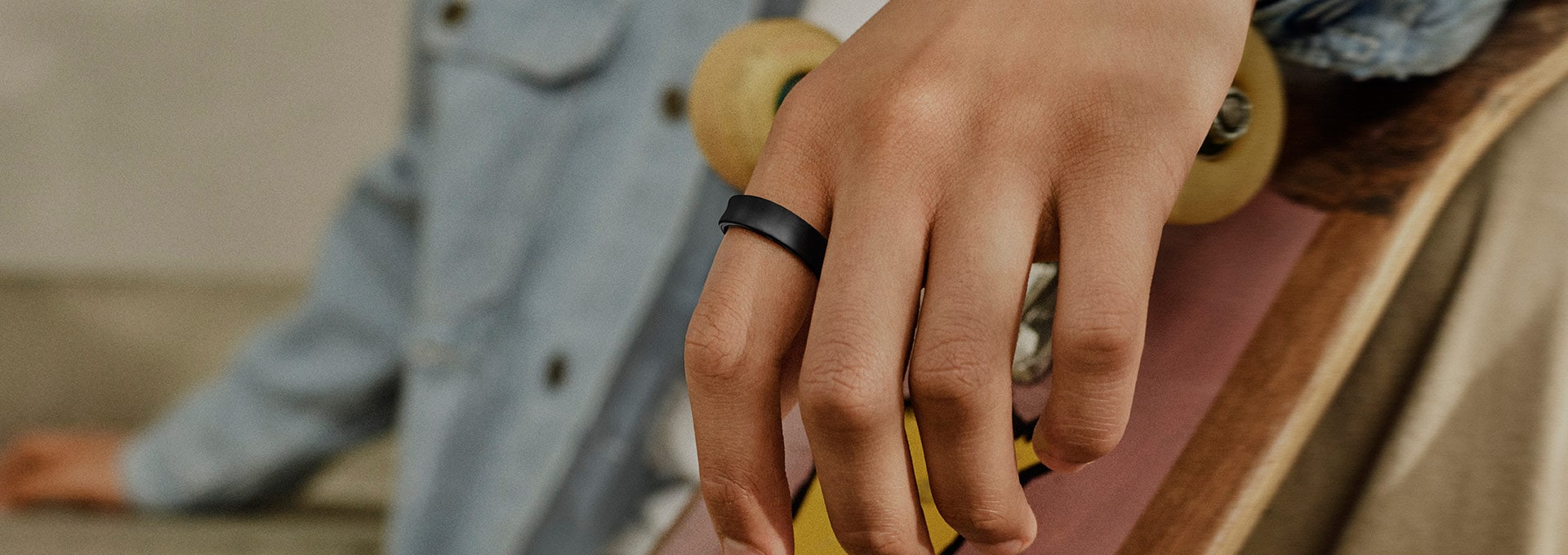 Виждаме близък план на ръка с Galaxy Ring на пръста и скейтборд на заден план. Това показва, че човекът е скейтбордист.