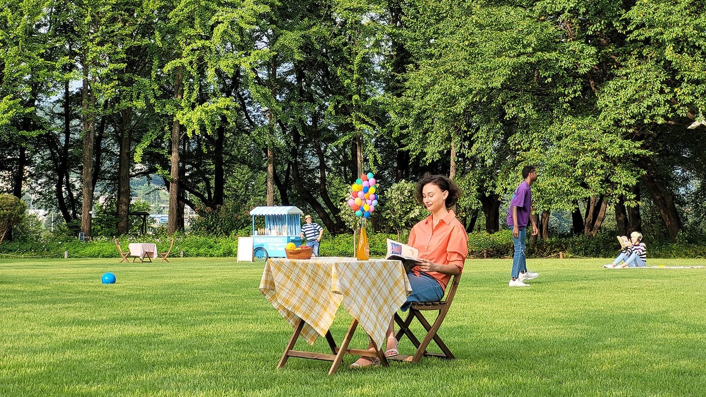 Foto con zoom de 3x de una mujer sentada sola en una mesa, en el fondo de la foto con zoom de 1x.