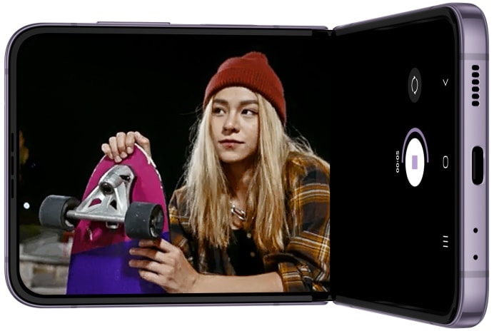 Se ve el Galaxy Z Flip4 en modo Flex. En la pantalla principal, se ve la aplicación de la cámara grabando un video de patinadores por la noche. Los sujetos son claros y el video es fluido, incluso con poca luz.