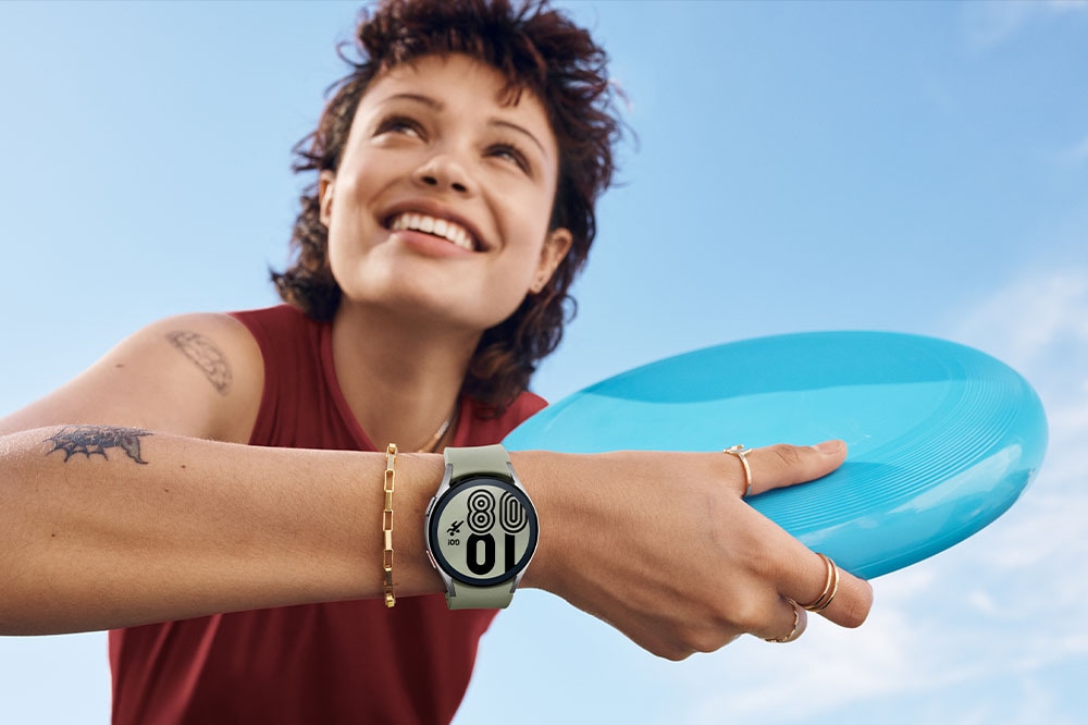 Una mujer sonríe y sostiene un frisbi mientras lleva un Galaxy Watch4 en plateado en la muñeca.