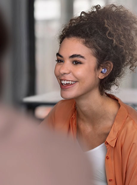 Una mujer con Galaxy Buds Pro en un café, hablando con alguien frente a ella con Voice Detect. Se acerca solo a ella para representar Ambient Sound.